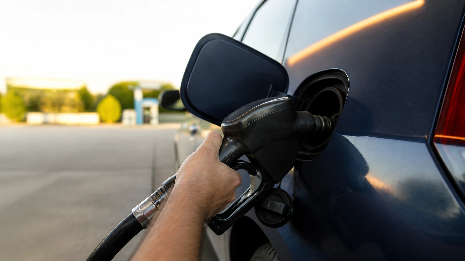 Mão segurando o bico de combustível encaixado no bocal do tanque de um carro durante o abastecimento